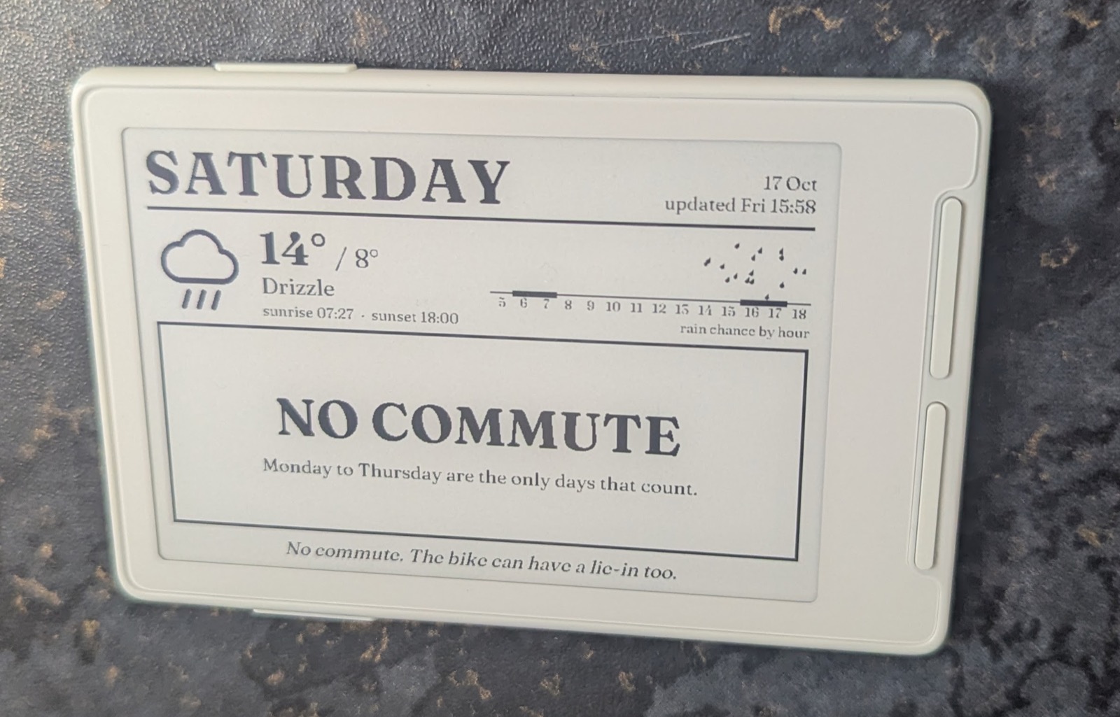 The Xteink e-reader in its cream case, showing SATURDAY, 14 degrees, drizzle, and NO COMMUTE in large serif capitals